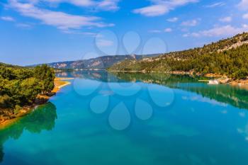Smooth emerald green water of Lake Sainte-Croix-du-Verdon reflects the sky and wooded shore. Mountain canyon Verdon in the French Alps