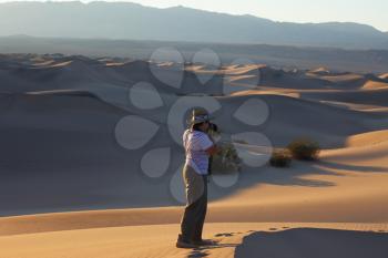 A magnificent sunrise amongst the sand dunes. Woman photographer in a striped T-short photographing sand waves