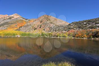 Bright autumn colors landscape. Mountains covered with orange and yellow bushes are reflected in the clean and clear water lakes