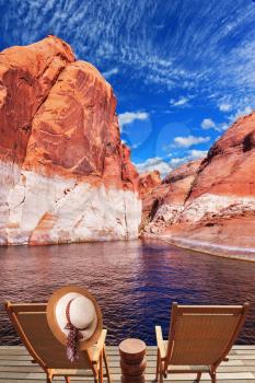 Walk to the tourist boat on Lake Powell on the Colorado River. At the stern of the vessel are two deck chairs. On the back of one hanging elegant ladies straw hat.