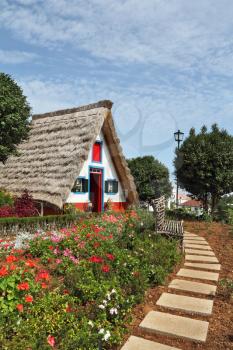 Cosy chalet with a triangular thatched roof. Before the house - garden with beautiful flower beds. Madeira Island, the city Santana