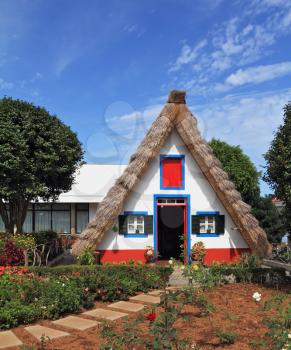 Pastoral landscape. Cosy chalet with a triangular thatched roof. Before the house - garden with beautiful flower beds. Madeira Island, the city Santana