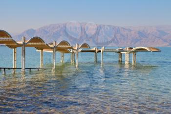 Sunny beach on the Dead Sea. A wonderful warm day in December. The beach pavilion is half flooded with seawater risen. Clearly seen the opposite shore of the sea - Jordanian mountains