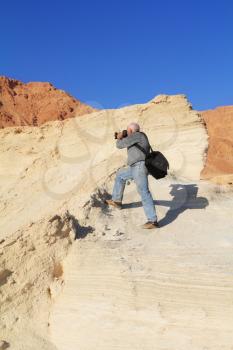 An elderly white-haired man with a passion photographs. Yellow clay canyon in Dead Sea