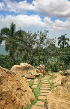 Masterpiece of landscape design - huge and fine park in Thailand. Palm trees, stone boulders and the path which has been laid out by tiles
