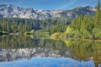 A lovely shallow lake in the mountains of California. In the smooth water surface reflects the majestic mountains and pine forests