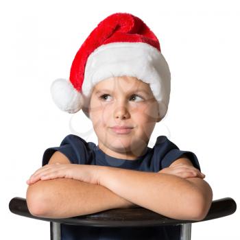 Charming seven year old boy in a red Santa hat looking up thoughtfully. Photo executed isolated