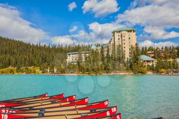 Lake Louise on a beautiful sunny day. At the pier moored red canoe for tourists. The lake is surrounded by pine forests