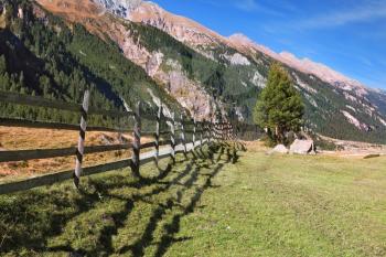  Alpine Valley in Austria. Headwaters National Park Krimml waterfalls.  Scenic farm fields blocked bythe wooden fence. Steep mountain slopes overgrown with coniferous forests