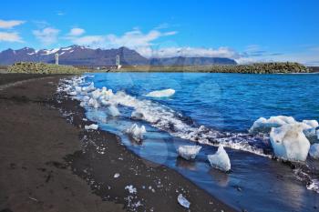 Ocean surf on the beach with black sand. Ice floes in the sun shine
