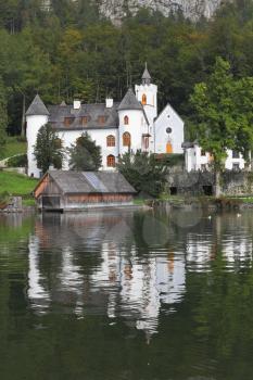 Abbey on the shore of Lake Hallstatt. White buildings are reflected in the smooth water of the lake