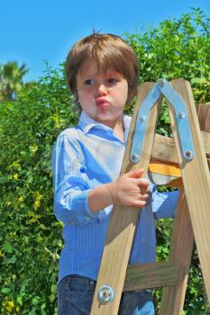 The beautiful green-eyed boy spoiled by attention climbed up a wooden sliding ladder