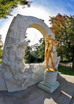 Elegant gilded statue of Johann Strauss, playing the violin in white marble arch. Park in Vienna