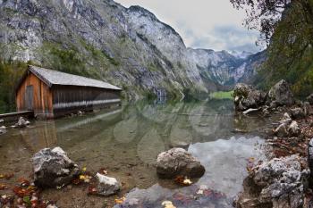 Cloudy day at Lake Koenigssee. Boathouse connected to the coast wooden decking. Clouds and mountains reflected in the water