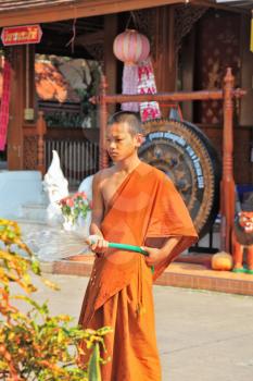 CHIANG MAI, THAILAND - APRIL 14, 2011:  Young Buddhist monk from a hose watering the flowers