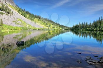 The majestic mountains and pine forests are reflected in the smooth water. A quiet lake in the mountains of California.