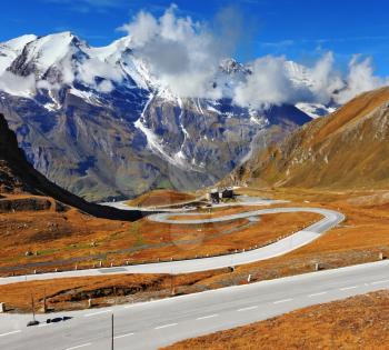 The well-known picturesque specific road in the Austrian Alps - Grossgloknershtrasse. Idealnoye Highway curls highly in mountains. The highest mountain tops are covered with fresh snow