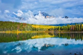 Charming Patricia Lake amongst the evergreen forests, yellow grass and distant mountains. Warm autumn in the Rocky Mountains of Canada