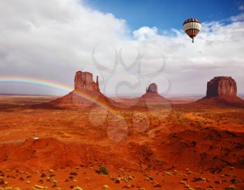 Huge balloon flies over Red Desert Navajo, USA. The picturesque rainbow crosses some rocks - mittens. On the road is a white jeep