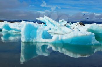 Blue and emerald icebergs and ice floes are reflected in smooth water of the Gulf Jökulsárlón in Iceland. Sunrise.