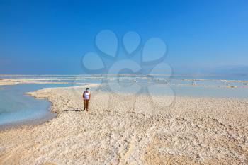 Path of the evaporated salt. The coast of the Dead Sea in Israel. The woman - tourist walks under the bright sun