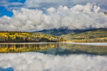 Patricia Lake. Adorable little lake surrounded by yellow and orange autumn grass and trees. Picturesque clouds are reflected in cold water. Jasper National Park in Canada