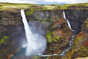  Vertical cliff, from which the powerful waterfall flies on black stones. Hayfoss dangerous waterfall in Iceland