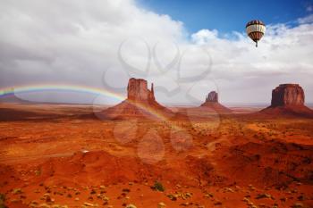Huge balloon flies over Red Desert Navajo, USA. The picturesque rainbow crosses some rocks - mittens. On the road is a white jeep