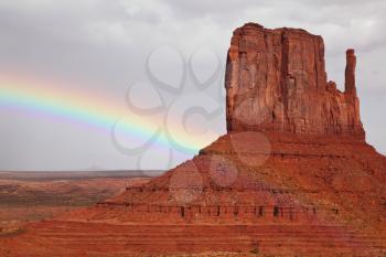 Navajo Reservation in the US. Red Desert and rocks - mitts sandstone. Huge rainbow crosses the cloudy sky