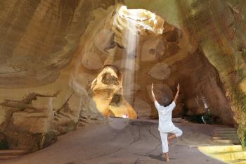 Belfry Caves of Beit Guvrin, Israel.  The slender elderly woman in a white suit for yoga carries out an asana Tree.