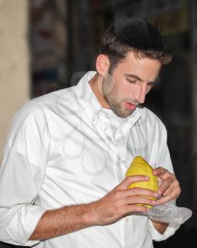 BENE - BERAK, ISRAEL - SEPTEMBER 17, 2013: Young religious man - Jew closely examining citrus - fruit for the holiday of Sukkot. The traditional holiday bazaar before Sukkot