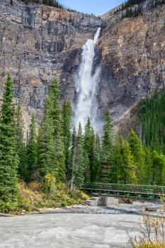 Small footbridge across the turbulent river.  Waterfall Takakkaw in Yoho National Park in the Rocky Mountains