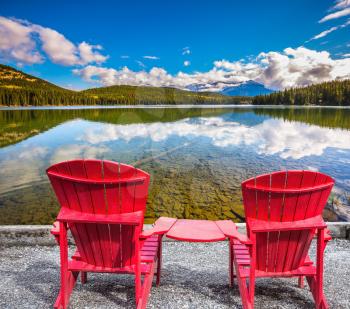 Pyramid Mountain reflected in Pyramid Lake. Two comfortable red deck chairs to tourists, interconnected table