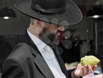 JERUSALEM, ISRAEL - SEPTEMBER 18, 2013: Traditional market before the holiday of Sukkot. The religious Jew with a long gray beard  very carefully examines ritual citrus - etrog