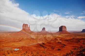 Red stone desert Navajo, USA. Isolated rocks - mitts intersect with the beautiful rainbow. On the road is a white jeep