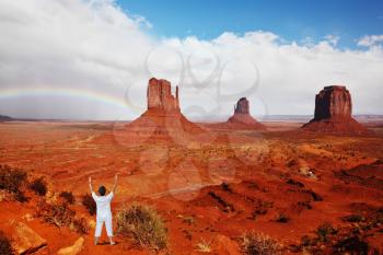 Woman in white performs asana Sun salutation under a huge rainbow. Navajo Reservation in the US. Red Desert and rocks - mitts sandstone