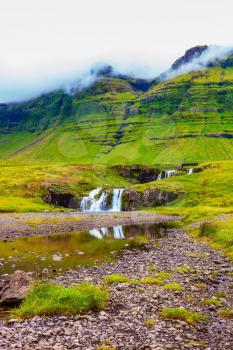 Cloudy day in Iceland. Mountains and waterfalls. Cascade Falls on the green grassy hill