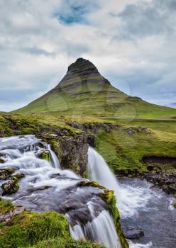Iceland - country of mountains, rivers and waterfalls. Threaded full-flowing waterfall Kirkyufell Foss on the grassy mountains