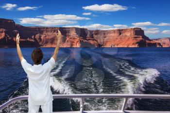 Middle-aged woman in white at the stern of the ship admiring the beauty of nature. Artificial lake Powell on the Colorado River, USA. The lake is surrounded by picturesque beaches of the orange sandst