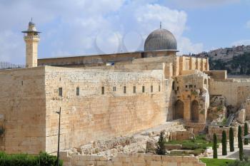 The ancient walls of Jerusalem, lit morning sun. Gray dome of the Al-Aqsa Mosque on the Temple Mount in Jerusalem