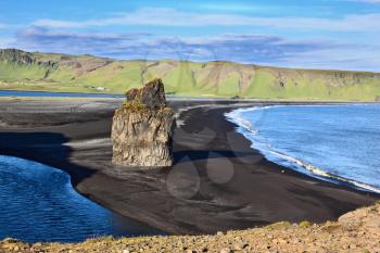 Cape Dirholaey in southern Iceland. On the beach with black volcanic sand is a huge rock in the shape of palms