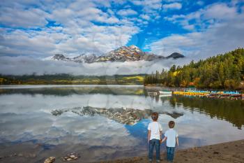 Two boys looking at a lake holding hands. Cloudy morning in the Rocky Mountains, Jasper Park. The concept of leisure and tourism