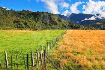 Countryside in Chilean Patagonia. Green field fenced low fence. Mountain range is visible in the distance