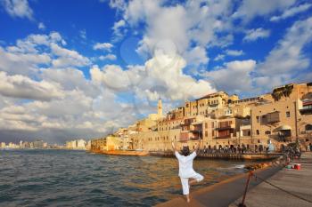 Sunset over the Old Jaffa in Tel Aviv. Fishing jetty port,  the woman in white performs asana Tree on one leg