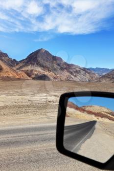 A great American roads. Road in dry and desert wildlife in Death Valley is reflected car mirror
