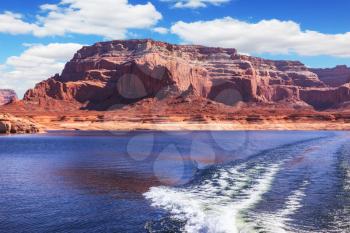  Foamy trace of motorboat crosses the emerald waters. Red sandstone hills surround the lake. Lake Powell on the Colorado River