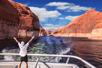 Man in  white shirt on the stern boat fascinated by nature. Artificial lake Powell on the Colorado River, USA. The lake is surrounded by picturesque beaches of the orange sandstone