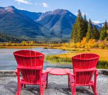 Concept of ecological tourism. Two comfortable red deck chairs on the lake. Indian summer in the Rocky Mountains of Canada