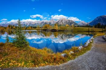 Path around the lake. The concept of recreational tourism. Canmore, near Banff National Park. Majestic mountains and scenic cumulus clouds are reflected in the water