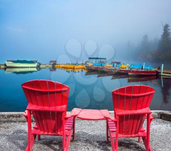 Two red comfortable sun loungers are on the Pyramid Lake. Foggy morning. Boat station waiting for tourists. Concept of vacation and tourism